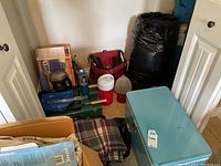Various camping items including cooler, sleeping mat, propane tank, lantern, skewers, and camp stove seen in basement corner