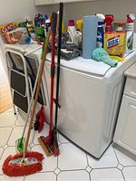 Photo of cleaning tools including mops, broom, step ladder, and various bottles on appliance surface.