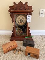 Overall view of antique wooden mantel clock with decorative boxes and clock keys arranged on carpet.