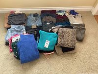 Full assortment of folded clothing showing various jeans, pants, tops, sweaters, and scrubs in multiple colors and patterns