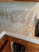 Several crystal and glass wine, champagne, and liqueur glasses arranged on kitchen countertop tiles. The photo shows varying sizes and intricate cut patterns.