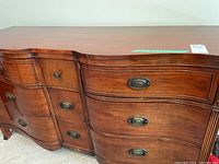 Front view of nine-drawer vintage wooden dresser showing curved design and brass handles.