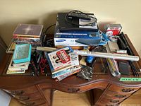 Wide view of DVD player, DVDs, office supplies, and decor arranged on a wooden dresser.