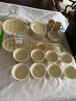 Full view of porcelain serving set arrayed on white cloth, showing multiple plates, bowls, cups, and a metal 3-tiered tray server with elaborate cutout design.