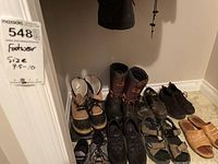 Photo showing nine pairs of men's footwear including boots, sandals, and shoes arranged against a wall.