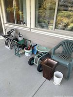 Photo showing the full set of garden tools, buckets, wheeled seat, two chairs, and pots arranged on a porch floor.