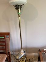 Full view of the tall brass floor lamp with decorative glass top and heavy base near chairs.