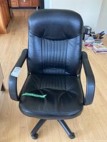 Front view of black office chair showing padded armrests, vertical stitched seat and backrest, wheel base.