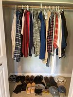 Full view of closet with men's outerwear and shirts hanging plus various shoes, hats, gloves, and glasses on floor under closet rod.