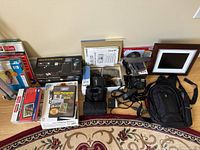 Photo showing Canon digital cameras, camera bag, binoculars, digital photo frame and various photography books and accessories arranged on carpet.