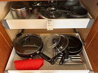 Upper cabinet drawer with various pots, pans, and lids including non-stick frying pans and a baking tray.