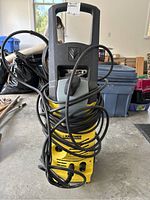 Front view of yellow and black Karcher power washer with power cords wound around the handle and base.
