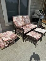 Full view showing dark brown rattan loveseat with floral cushions and two ottomans with matching cushions outdoors