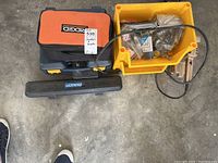 Overview of lot showing Ridgid sander, drill carrying cases, yellow plastic bin with accessories, and Lazerpro laser level case.