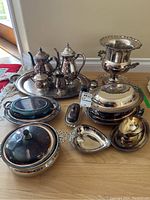 Overall photo of assorted electroplated serveware pieces including trays, tea and coffee pots, chiller bucket, covered dish, cooler, and small serving dishes