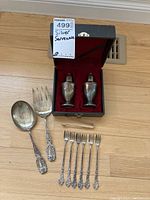 Full view of all pieces laid out including salt and pepper shakers in box, serving spoon, serving fork, ice tongs, and six forks.