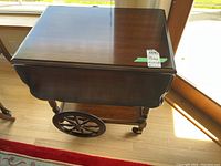 Full view of wooden tea trolley from above showing polished top with drop-leaf sides and large spoked wheels.