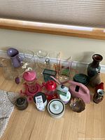 Wide shot showing the full assortment of items including glass vases, pitchers, red hummingbird feeders, and ceramic decorative pieces on a floor against the wall.