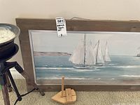 Wall with large framed canvas art showing sailboats on water, small wooden boat model on the floor, and candle on metal stand
