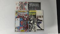 Top view of seven Spider-Man related comic books, some with protective sleeves. Notable visible titles include Spider-Man Unlimited and Spider-Man Reign.