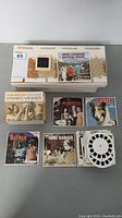 Display of View-Master Standard Stereo Viewer in original box, multiple reels including those featuring Royal Canadian Mounted Police, The Munsters, Lassie, Batman, Lone Ranger, and others, plus some random slides.