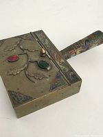 Top view of the brass coal iron showing enamel and colored stone decorations on the lid and detailed handle.