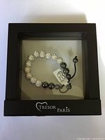 Front view of the Tresor Paris bracelet inside black box, showing bead details and tag.