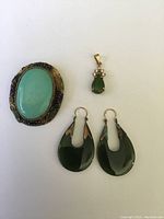 Front view of turquoise brooch, jade pendant, and earrings on white background