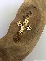 Gilt sterling silver cross pendant with intricate cut-out design lying on a piece of wood, showing front side detail and loop for chain attachment.