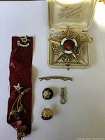 Photo showing the complete lot of military pins and badges arranged on a white background including a large star medal in a box, a red ribbon with multiple pins, and individual pins placed below.