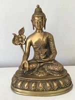 Front view of the antique Buddha statue showing facial details, hand positions, flower on the side, and base design.