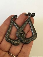 Close-up front view of one earring showing the teardrop shape, etched decorative patterns and black enamel surface.