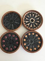 Four round wood and ceramic coasters shown from the top with mid century modern design patterns in black with orange and red dots.
