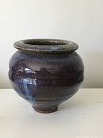 Side view showing rounded squat shape, thick rim, and dark glossy glaze with subtle color variations.