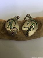Pair of oblong sterling silver earrings with a cutout abstract dancing figure inlaid with colorful abalone shell, showing front design and screwback clasps.