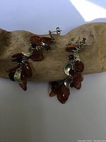 Pair of amber and silver dangle earrings displayed on driftwood showing cluster design and silver elements.