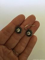 Pair of sterling silver drop earrings with clear round gemstones shown against a neutral background held in hand.