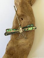 Front view of sterling silver dragonfly brooch showing abalone shell wings and central body piece on wood background.