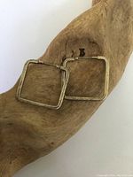 Pair of tarnished sterling silver square-shaped hoop earrings resting on a wooden surface. Earrings have a simple design with a hinged clasp.