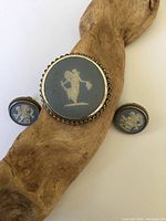 Front view of the Wedgewood brooch and earrings on wooden stand showing blue pottery centers with white classical figures and twisted silver borders.