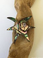 Front view of starfish brooch showing colorful abalone shell inlay and silver edges, placed on wooden surface.