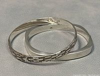 Two sterling silver bangles on textured surface, showing different designs and condition.