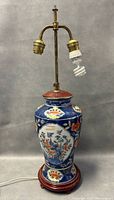 Full view photo of the Chinese hand painted porcelain vase lamp showing the wooden base, brass fixture with two light bulb sockets, and one spiral bulb attached.