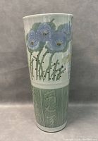 Front view of the tall hand painted vase showing blue flowers and green stems on upper half, and abstract green pattern on lower half.
