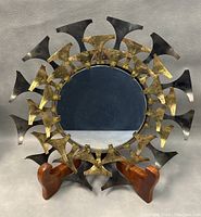 Front view of the round mirror showing black and gold-tone sunburst iron elements around reflective glass mirror surface on wooden stand.