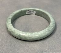 Top view of the polished greenish gray jade bangle showing its round shape and natural color variations.