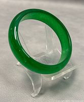 Green jadeite bangle displayed on clear acrylic stand