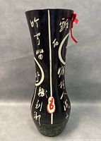 Front view of black vase with vertical white calligraphy and red seal mark with a red ribbon tied at the neck.