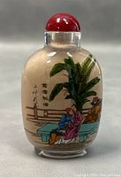 Front view of reverse painted Chinese snuff bottle featuring two seated figures with a lush plant and Chinese characters.