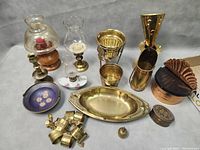 Photo showing vintage brass candle holders, glass vases with brass bases, a blue floral dish, brass tray, wooden and copper lidded container, small brass decorative items and napkin rings.